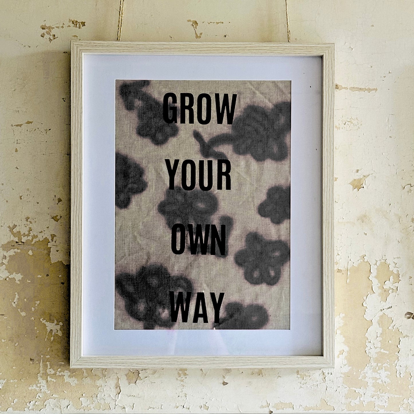 Framed print with motivational 'Grow Your Own Way' text on a linen fabric against a textured wall.