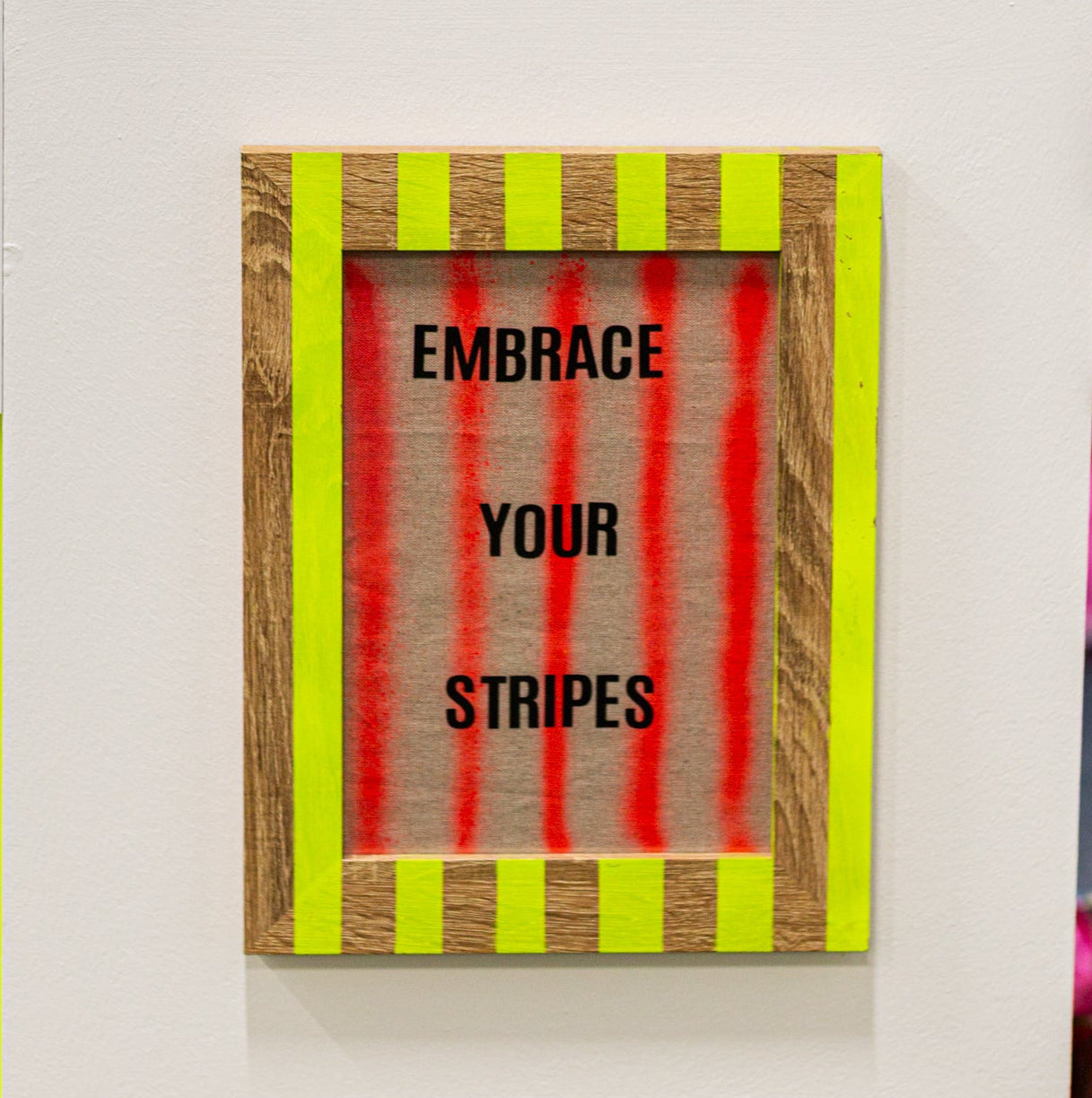 handprinted stripe wooden frame  with a motivational sign reading 'Embrace Your Stripes' on a white wall