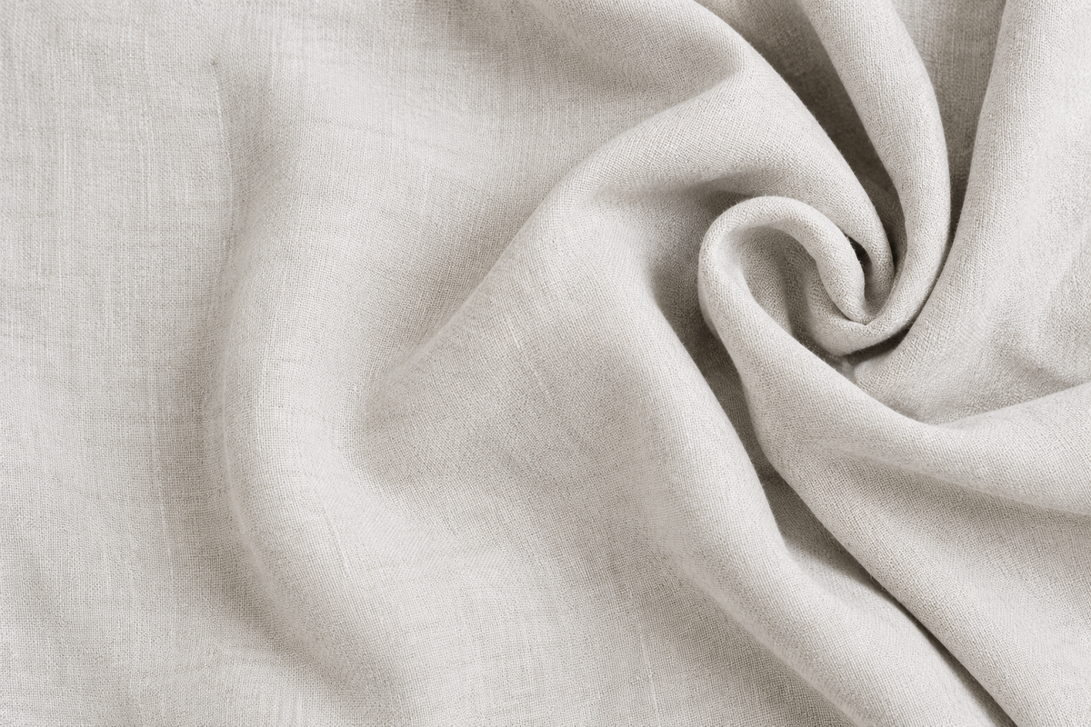 A close-up of draped off-white linen and cotton fabric with a soft, textured weave, arranged in gentle folds and swirls.