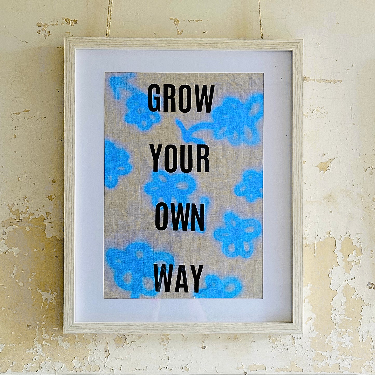 Framed print with motivational 'Grow Your Own Way' text on a linen fabric neon blue flowers