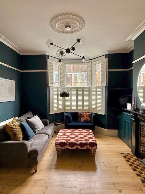 Living room with dark blue walls, gray sofa, and patterned ottoman.
