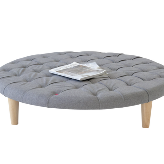 Round gray upholstered cushioned ottoman with wooden legs on a white background